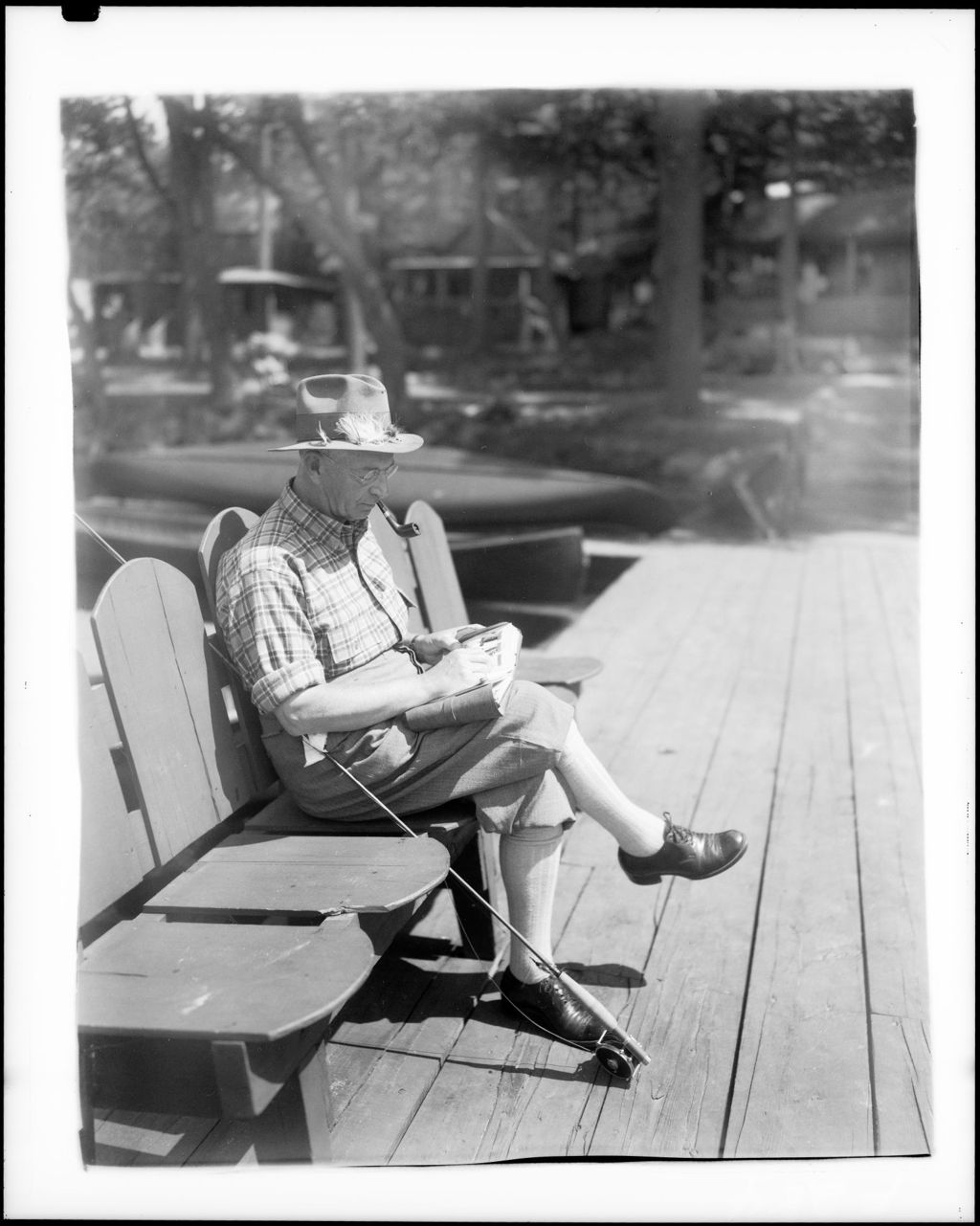 Miniature of Man Sitting In Chair On A Dock Reading A Book, Fishing Rod On Dock Beside Him