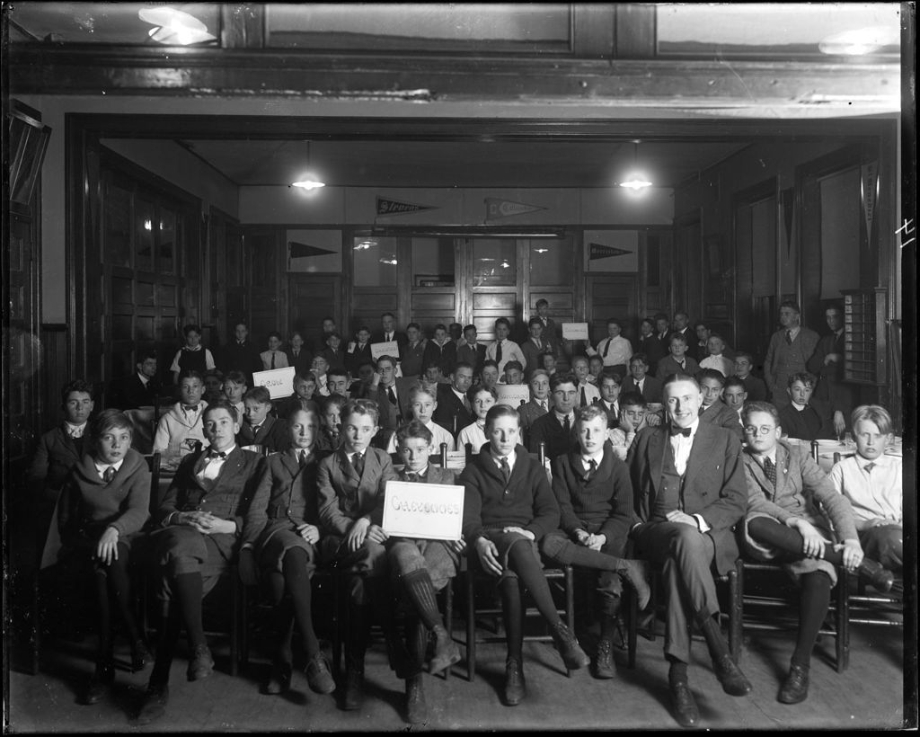 Miniature of Many Young Men (Boys) Gathered Together In A Room Grouped With Signs Bearing Native American Tribe Names