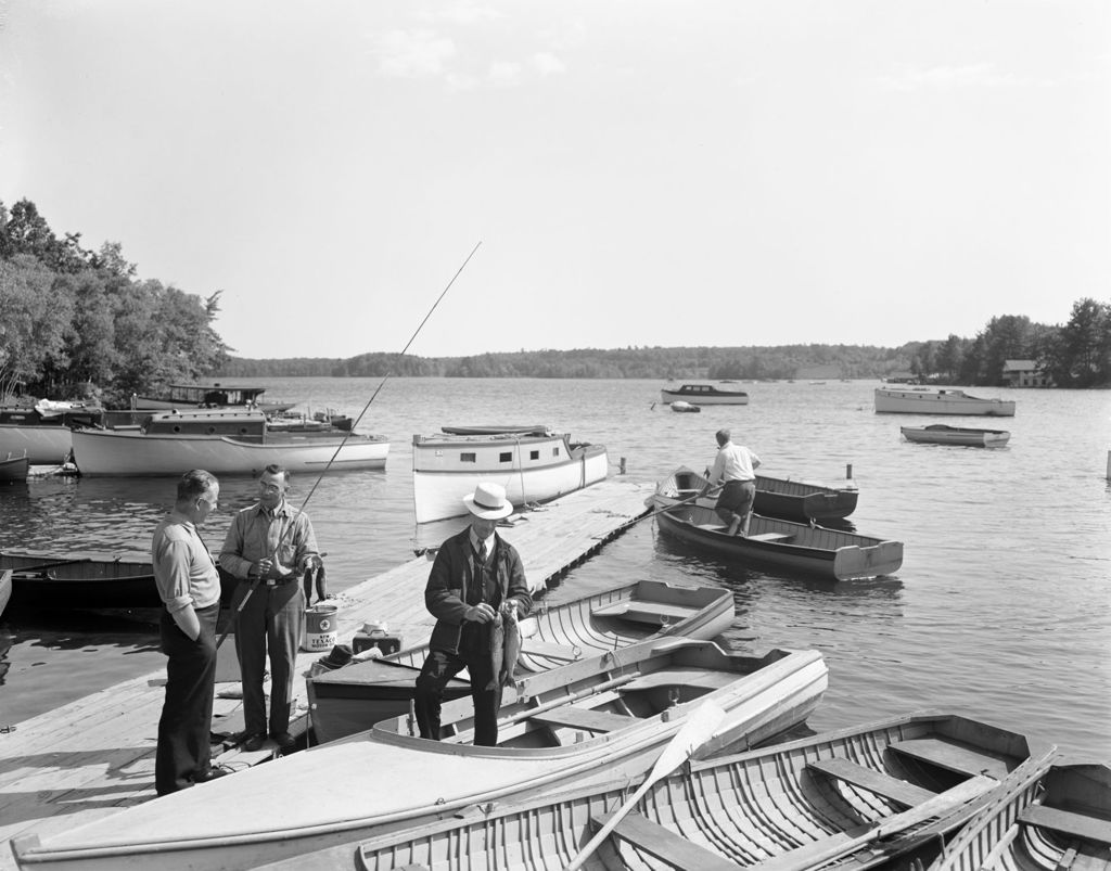 Miniature of Two Men On A Dock Talking, One Man In A Boat Holding Fish He Caught, Another Man Getting Ready To Go Fishing At Sebago